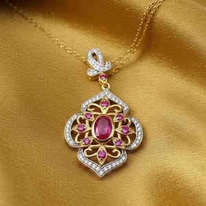 May include: A gold-toned pendant necklace with a floral design. The pendant features a large oval ruby center stone, surrounded by smaller pink gemstones and clear crystals. The necklace is displayed on a gold satin fabric.