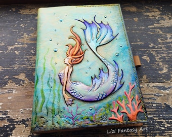 May include: A leather-bound journal with a hand-painted mermaid design. The mermaid has a purple tail and red hair, and is surrounded by green seaweed and red coral. The journal is titled "Lizi Fantasy Art".