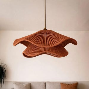 May include: A hanging, layered pendant light fixture in a warm terracotta color. The light has a unique, wavy design with a textured, woven appearance. The fixture is suspended from a thin, brown cord and is a decorative element for interior spaces.
