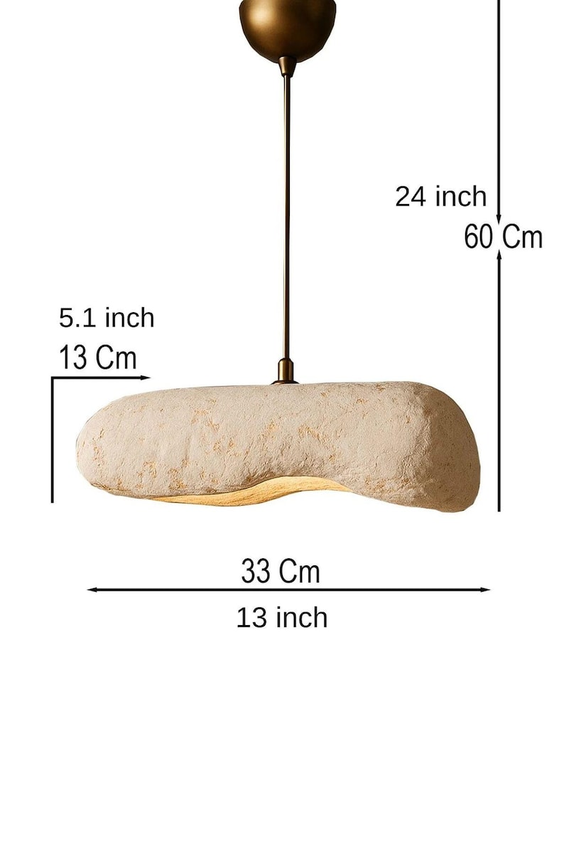 K&ouml;nnte beinhalten: Beige, l&auml;ngliche Pendelleuchte. Die Leuchte ist 33 cm lang, 13 cm breit und h&auml;ngt 60 cm von der Decke. Die Leuchte hat eine strukturierte Oberfl&auml;che und ein messingfarbenes Baldachin.