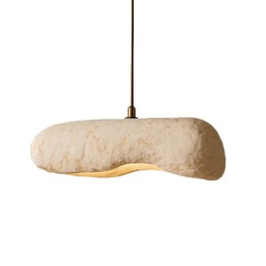 K&ouml;nnte beinhalten: H&auml;ngeleuchte mit einem strukturierten, l&auml;nglichen, cremefarbenen Schirm. Der Schirm h&auml;ngt an einem bronzefarbenen Stiel und einer Deckenhalterung. Die Leuchte hat ein modernes, minimalistisches Design. Ca. 40 cm lang.