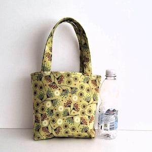May include: A small, light green tote bag with a floral pattern in brown, white, and blue. The bag has two handles and is next to a clear plastic water bottle.