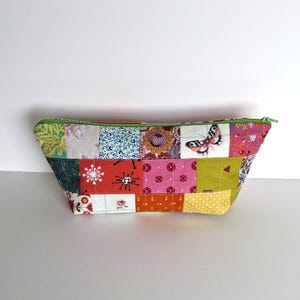 May include: A patchwork fabric cosmetic bag with a green zip. The bag is made of various colourful floral and patterned fabrics, including a butterfly print. The bag is rectangular with a slightly trapezoidal shape.