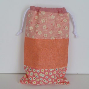 May include: A patchwork drawstring bag with a floral and textured design. The bag features a pink floral pattern at the top and bottom, with a textured orange centre. A white drawstring is visible at the top.