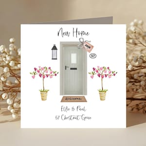 May include: A square card featuring a watercolour illustration of a front door, trees with heart-shaped leaves, and the text "New Home." The card includes the address "57 Chestnut Grove" and the names "Ellie & Paul."