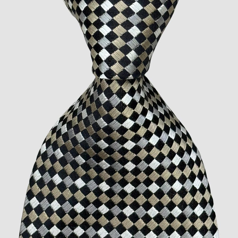 May include: A close-up of a necktie with a checkered pattern. The tie features a repeating design of black, silver, and tan squares. The tie is knotted at the top, showcasing the fabric's texture and design. The background is a solid, neutral color.