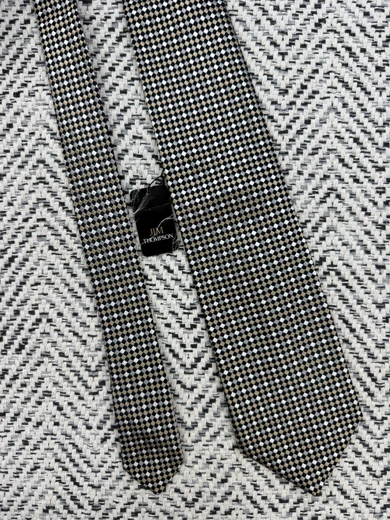 May include: A black, white, and tan checkered tie with a matching tie. The tie has a small, repeating square pattern. The tag reads "JIM THOMPSON".