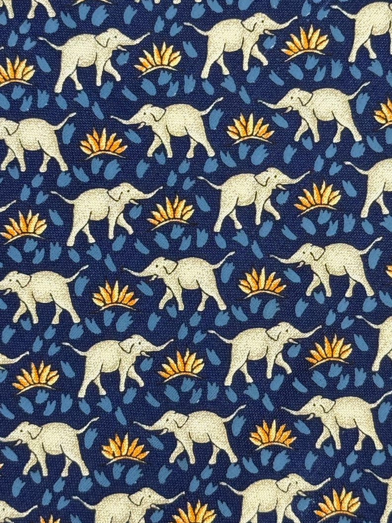 May include: A navy blue fabric featuring a repeating pattern of white elephants, orange floral shapes, and blue brushstroke-like designs. The elephants are depicted walking with raised trunks. The design is symmetrical and detailed.