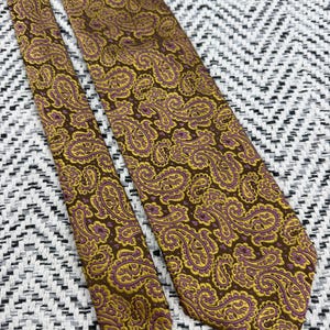 May include: A necktie featuring a detailed paisley pattern in shades of brown, gold, and purple. The fabric displays a repeating intricate design of teardrop-shaped motifs across the entire surface of the tie, including the narrow and wide ends.