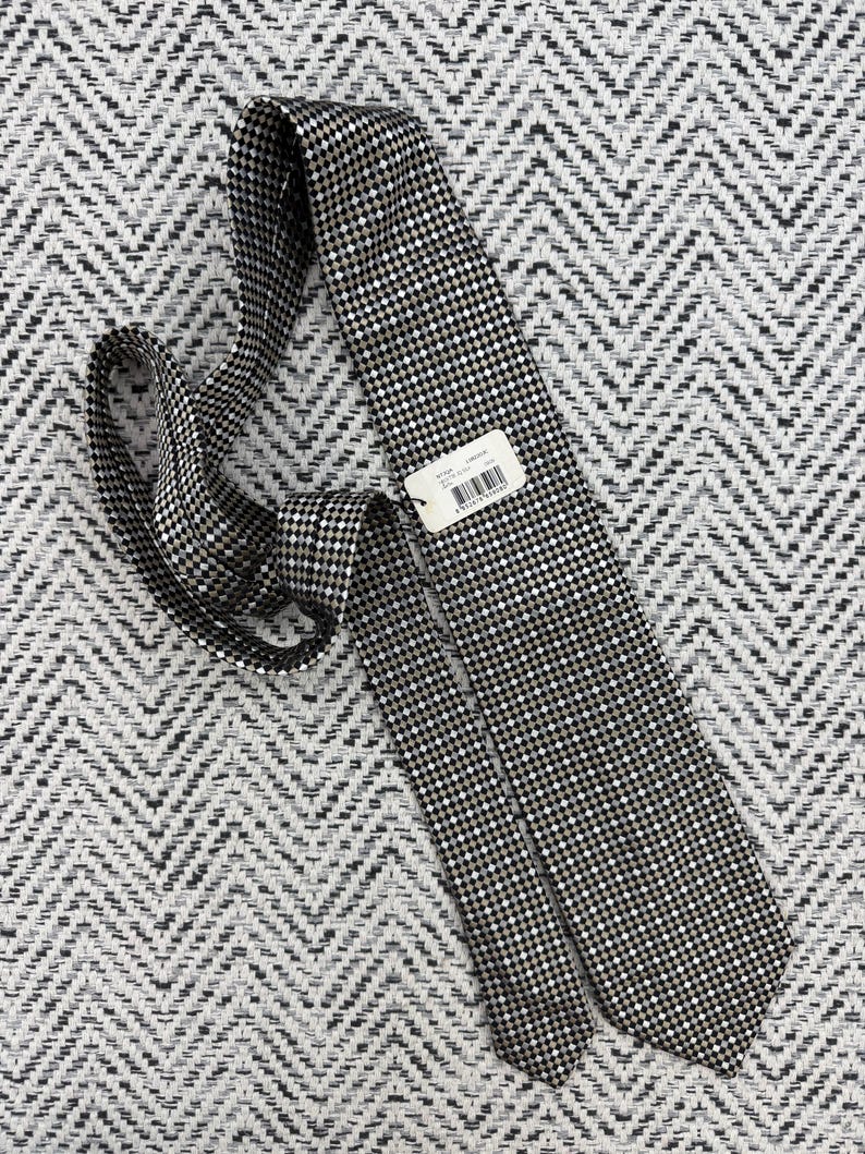 May include: A black and white checkered tie with a small tag attached. The tie is made of a woven fabric and is lying on a textured, patterned surface. The tie is a classic accessory.