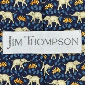 May include: A navy blue tie featuring a repeating pattern of beige elephants, orange and blue accents. The label reads "JIM THOMPSON".