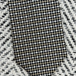 May include: A patterned necktie with a repeating checkered design in black, white, and tan. The tie is made of a smooth fabric and is displayed on a textured surface.