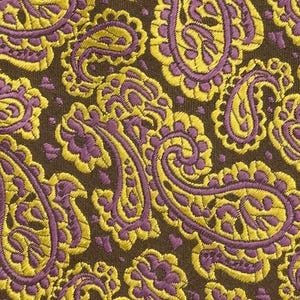 May include: A fabric featuring a dense, repeating paisley pattern in vibrant yellow and purple threads set against a dark brown background. The intricate, teardrop-shaped motifs are woven with a textured finish, creating a detailed surface.