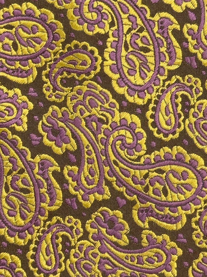 May include: A fabric featuring a dense, repeating paisley pattern in vibrant yellow and purple threads set against a dark brown background. The intricate, teardrop-shaped motifs are woven with a textured finish, creating a detailed surface.