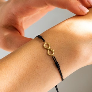 Puede incluir: Un brazalete de cuerda negra con un dije de infinito de oro.
