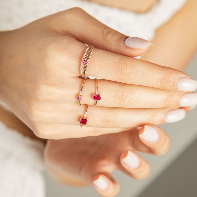 Op de afbeelding: Een hand met vier gouden ringen met rode edelstenen. De ringen zijn gestapeld op de middelvinger.