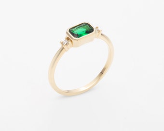 May include: A gold ring with a green emerald-shaped stone and two small clear stones.