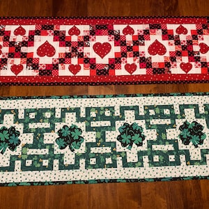 May include: Two table runners, one with a red and black heart pattern and the other with a green shamrock pattern.