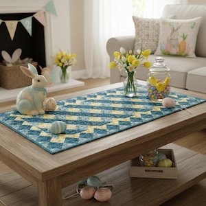 Peut inclure: Une table basse en bois avec un chemin de table à motifs bleus et jaunes. Les décorations de Pâques comprennent un lapin en céramique, des œufs peints et un bocal en verre rempli de poussins jaunes et de bonbons colorés. Un vase de fleurs jaunes est posé sur la table.