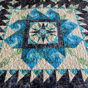 May include: A blue and white quilt featuring a compass design in the centre. The quilt is made from fabric with a star pattern and is quilted with a swirl design.