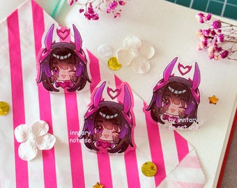 May include: Three clear acrylic charms featuring a cartoon character with purple hair and pink accents. The charms have a heart-shaped design on the head and are placed on a pink and white striped surface. Additional decorative elements include flowers and stars.
