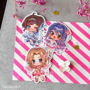 Könnte beinhalten: Drei Aufkleber im Anime-Stil mit Chibi-Charakteren mit großen Augen und farbenfrohen Outfits. Die Aufkleber befinden sich auf einem rosa-weiß gestreiften Hintergrund. Der Text "by inntary do not use" ist auf den Aufklebern zu sehen.