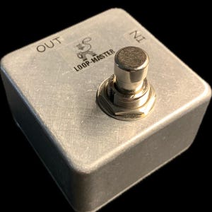 May include: A silver metal foot pedal with a single button labelled "IN" and "OUT". The pedal has the text "LOOP-MASTER" printed on it.