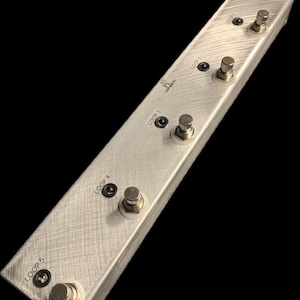 Könnte beinhalten: Ein silbernes Metall-Pedalboard mit fünf Fußschaltern, die mit "LOOP 1" bis "LOOP 5" beschriftet sind.