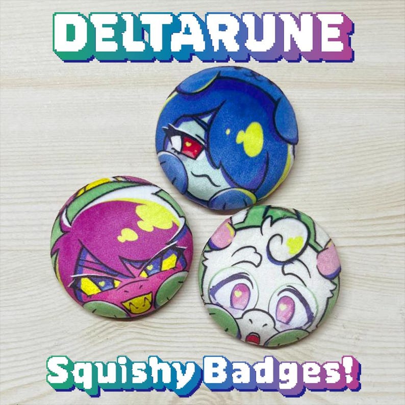 May include: Three round, squishy badges with colorful character designs. The top badge is blue with a face, the bottom left is purple with a face, and the bottom right is white with a face. The word "DELTARUNE" is at the top, and "Squishy Badges!" is at the bottom.