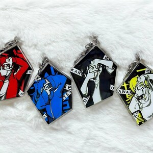 May include: Four keychains featuring anime characters with black and white, red, blue, and yellow designs. Each keychain has a different character with a unique design and text. The text on the keychains includes "RET", "SH", "YES", "DE", "AWAK", and "KO".