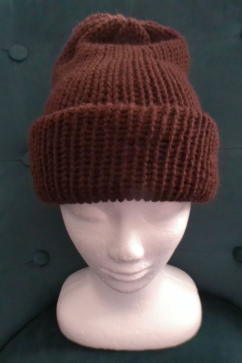 Puede incluir: Un gorro de punto marr&oacute;n sobre una cabeza de maniqu&iacute; blanca. El gorro est&aacute; hecho de un hilo grueso y texturizado y tiene un dise&ntilde;o simple y cl&aacute;sico.