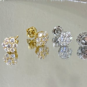 May include: Three round stud earrings with a pave setting of small clear stones. The earrings are shown in gold, silver, and white gold. The earrings are 8mm in diameter and have a total of 14 stones. The thickness of the earrings is 4.5mm.