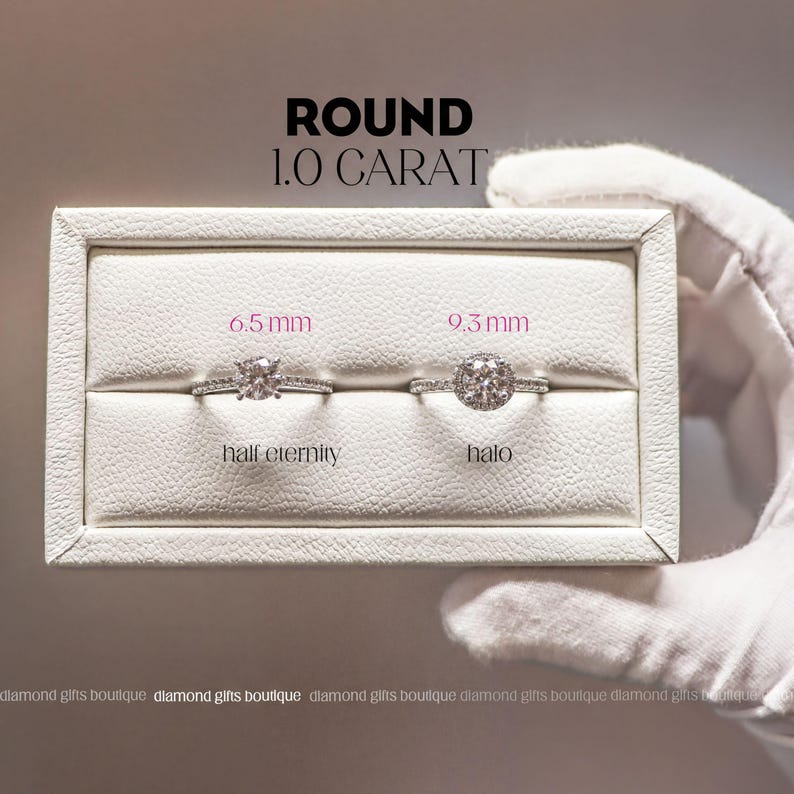a hand holding a white jewelry box containing two diamond rings, one labeled "half eternity" and the other labeled "halo". The box is placed on a white surface, and the background is blurred.