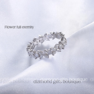 May include: A silver-colored ring with a floral design and clear gemstones. The ring is set against a white background. The text "Flower full eternity" is visible.