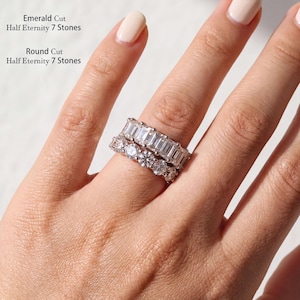 May include: Two silver-toned half eternity rings featuring seven stones each. The top ring has emerald-cut stones, and the bottom ring has round-cut stones. Text on the image reads: Emerald Cut Half Eternity 7 Stones and Round Cut Half Eternity 7 Stones.
