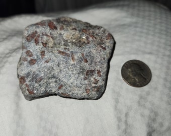 May include: A close-up of a gray and red rock with a rough texture. The rock is about the size of a quarter.