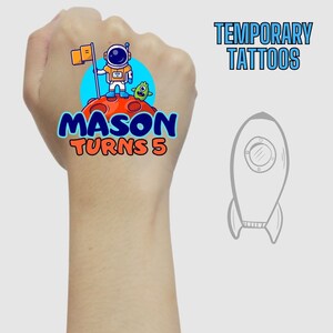Könnte beinhalten: Temporäre Tattoos mit einem farbenfrohen Astronauten-Design und dem Text "MASON TURNS 5" auf einem roten Planeten. Eine Cartoon-Rakete ist ebenfalls abgebildet. Geeignet für Kindergeburtstage.
