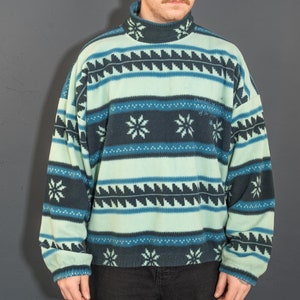 May include: A blue and black patterned fleece sweater with a mock neck. The sweater has a white snowflake design and the text "Overlooking the City of the Sky".