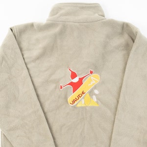 May include: A beige fleece jacket with a red and yellow embroidered logo of a person snowboarding with the word "VAUDE" on the back.