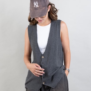 Puede incluir: Una mujer con un chaleco de punto gris, pantalones cortos de carga gris oscuro, calcetines blancos y zapatillas blancas con rayas negras. También lleva una gorra de béisbol gris con las letras "NY" bordadas en la parte delantera.