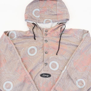Könnte beinhalten: Eine hellrosa und graue Kapuzenjacke mit einem weißen und grauen abstrakten Muster. Die Jacke hat einen Knopfverschluss und eine Kapuze mit Kordelzug.