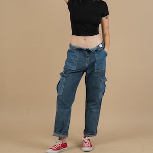 Könnte beinhalten: Eine blaue Jeanshose im Cargo-Stil mit mehreren Taschen und einer lockeren Passform. Die Hose ist an den Knöcheln umgeschlagen und das Model trägt rote Turnschuhe.