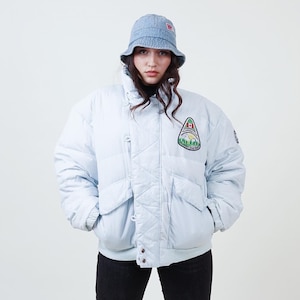 Könnte beinhalten: Eine hellblaue Steppjacke mit einem grünen, weißen und roten Aufnäher, auf dem "Campside" steht und eine kanadische Flagge abgebildet ist. Die Jacke hat einen Reißverschluss und zwei Taschen.