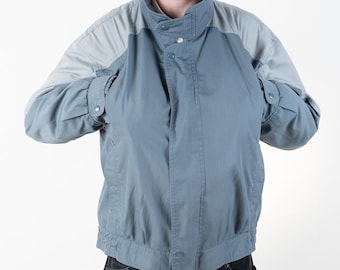 May include: A man wearing a blue and gray jacket with a zipper and button closure. He is wearing black corduroy pants.