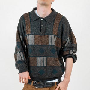 Könnte beinhalten: Ein grau, braun und türkis gemusterter Pullover mit Kragen und Knopfverschluss. Der Pullover wird mit einer braunen Hose und einem schwarzen Gürtel kombiniert. Das Outfit ist lässig und alltagstauglich.