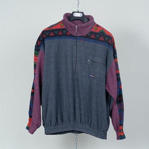 May include: A blue fleece jacket with a colorful geometric pattern on the sleeves. The jacket has a zipper closure and a small pocket on the left chest.