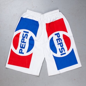 Op de afbeelding: Witte sport shorts met een rood en blauw Pepsi-logo op elk been.