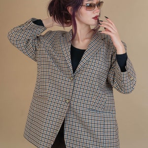 May include: A woman wearing a brown and blue plaid blazer with a black turtleneck shirt underneath. She is wearing sunglasses and has dark purple hair.