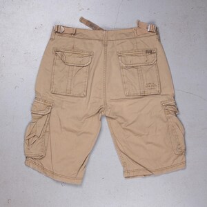 Könnte beinhalten: Beigefarbene Cargo-Shorts mit mehreren Taschen und einem Markenetikett auf der Gesäßtasche. Die Shorts haben Gürtelschlaufen und einen Knopfverschluss.