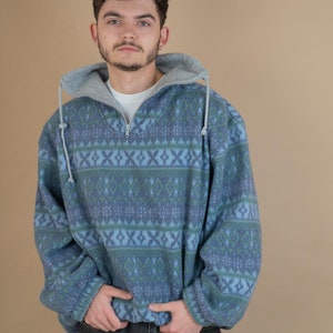 May include: A blue and green patterned fleece pullover with a grey hood. The pullover has a zip closure and a relaxed fit.